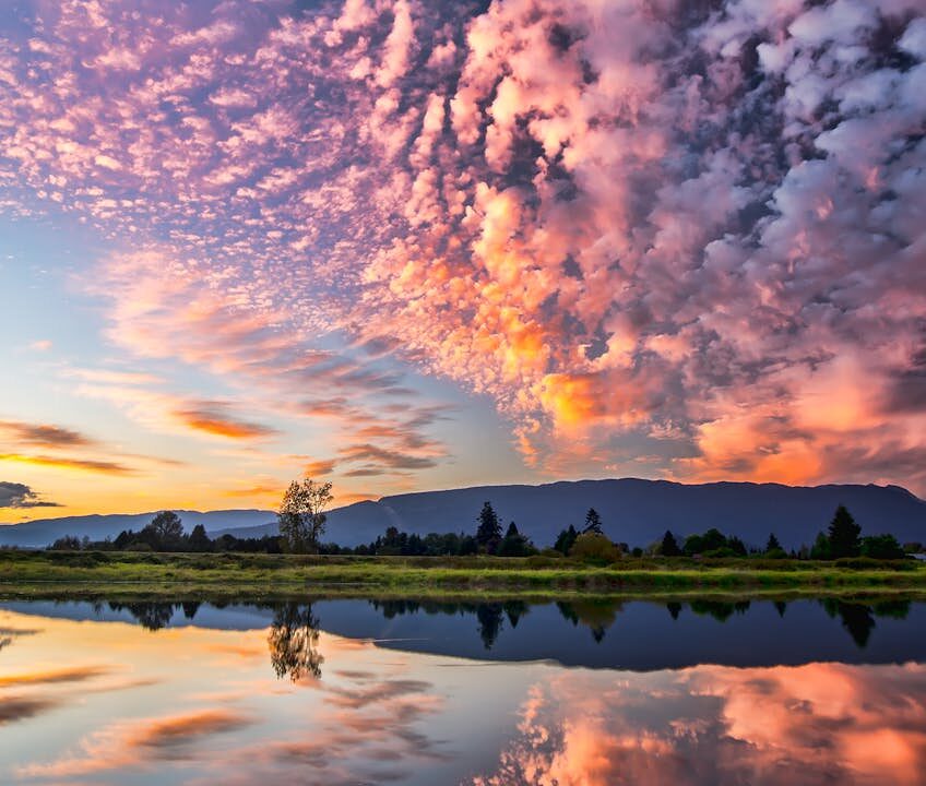 Captivating sunset with vibrant clouds and serene reflections over Pitt Meadows, BC.