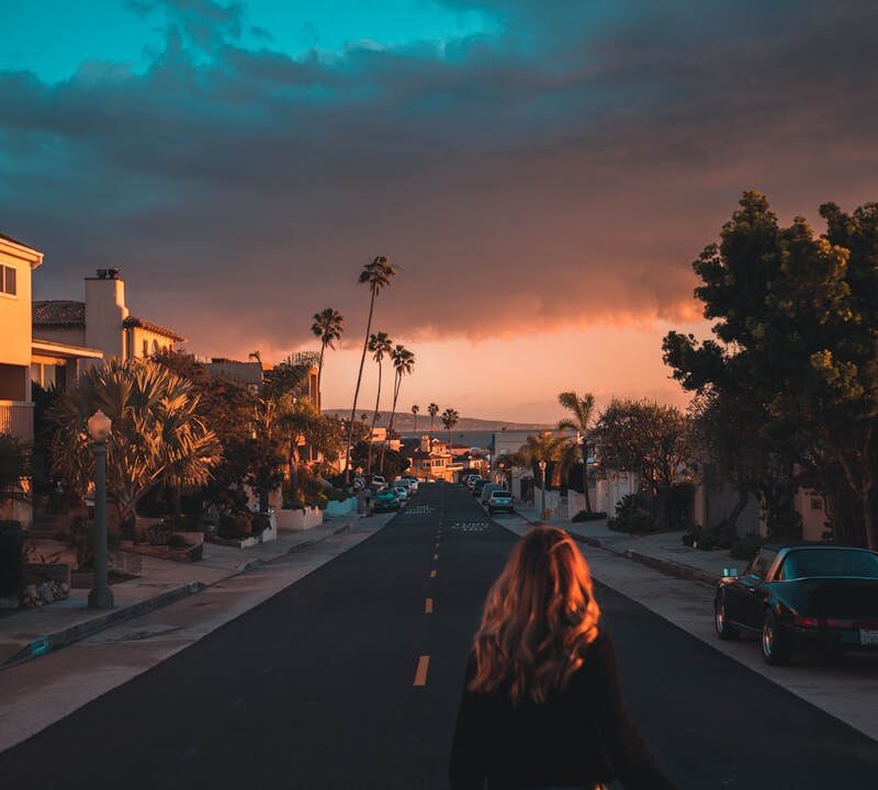 Woman walking on a Los Angeles street during a vibrant sunset with palm trees lining the road.