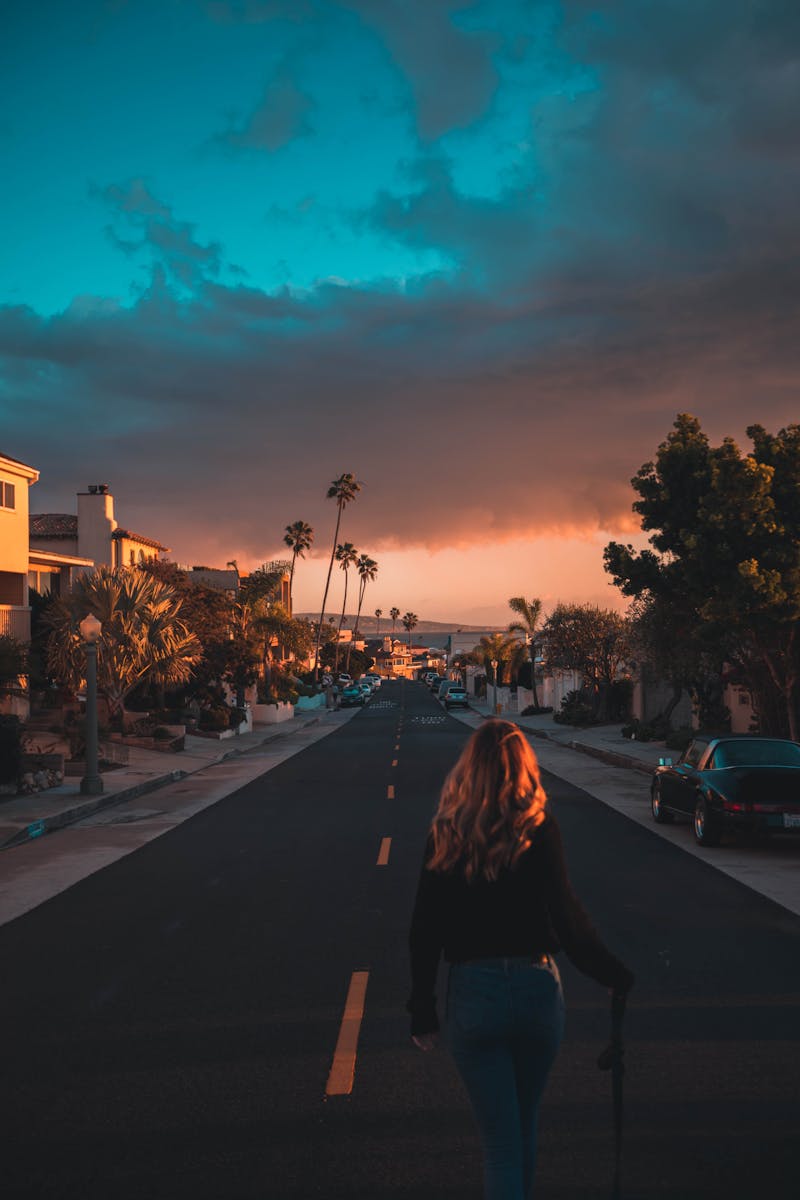 Woman walking on a Los Angeles street during a vibrant sunset with palm trees lining the road.