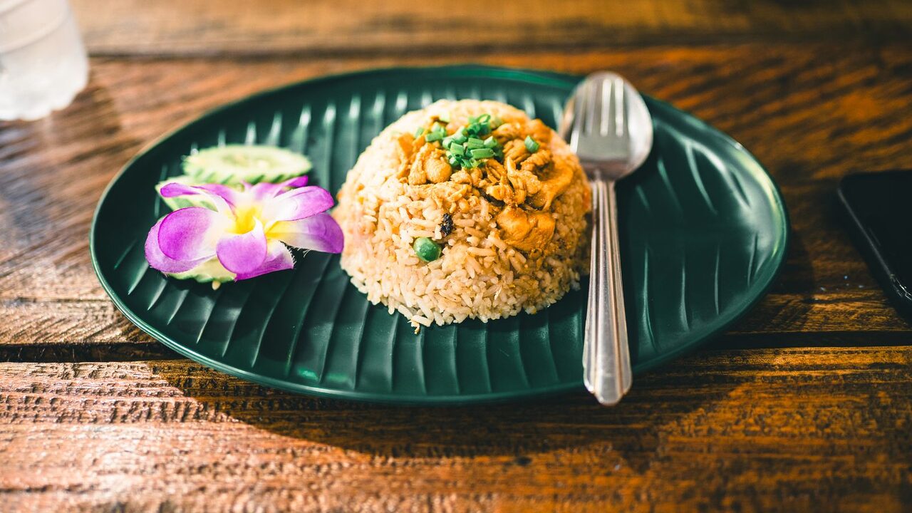 Delicious Thai fried rice served on a green plate, garnished with flower. Perfect for authentic Thai cuisine lovers.